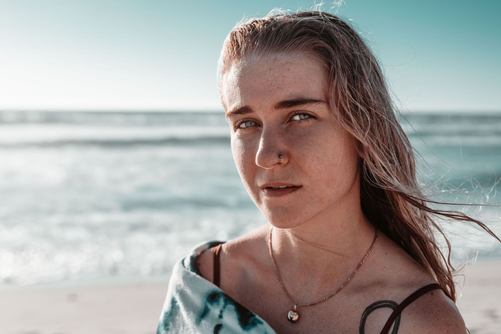 Girl wrapped in a tie dye towel wears a gold pendant after swimming in the ocean