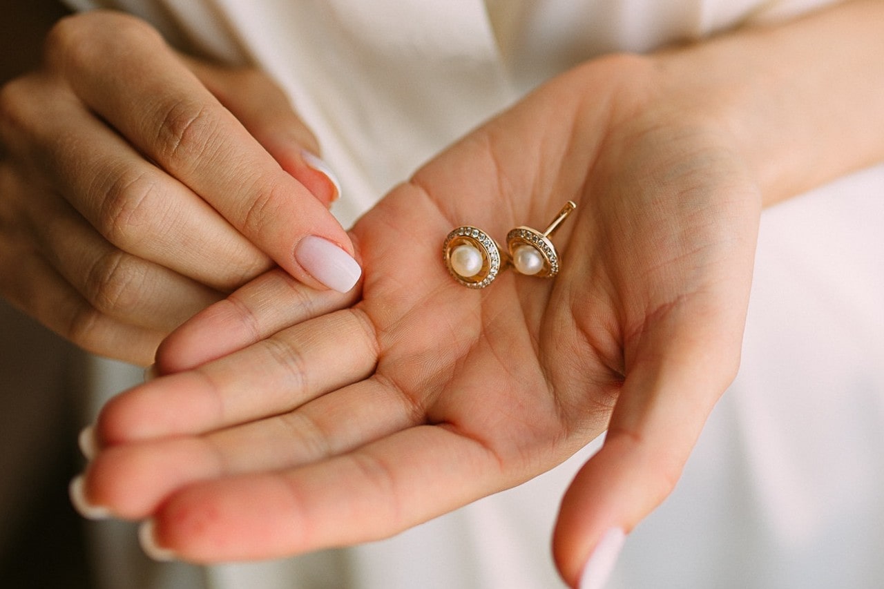 A woman with manicured nails holds yellow gold and pearl studs to examine them for damage
