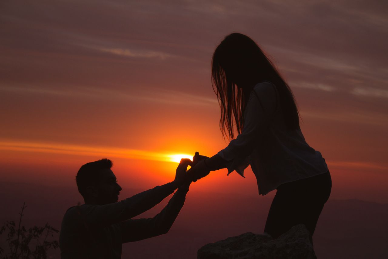 A man proposing to a woman at sunset on the peak of a mountain