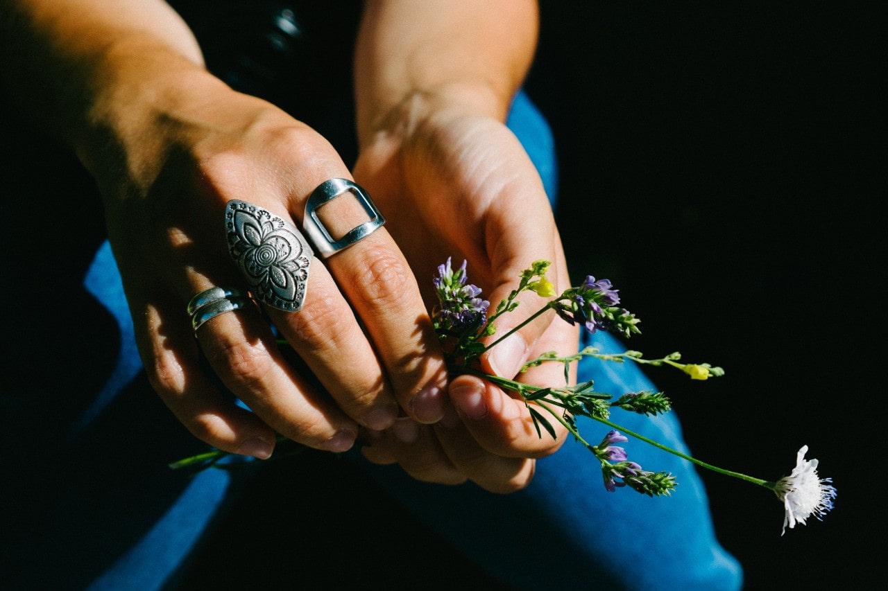A person holding a few wildflowers while wearing three sterling silver rings with exciting designs