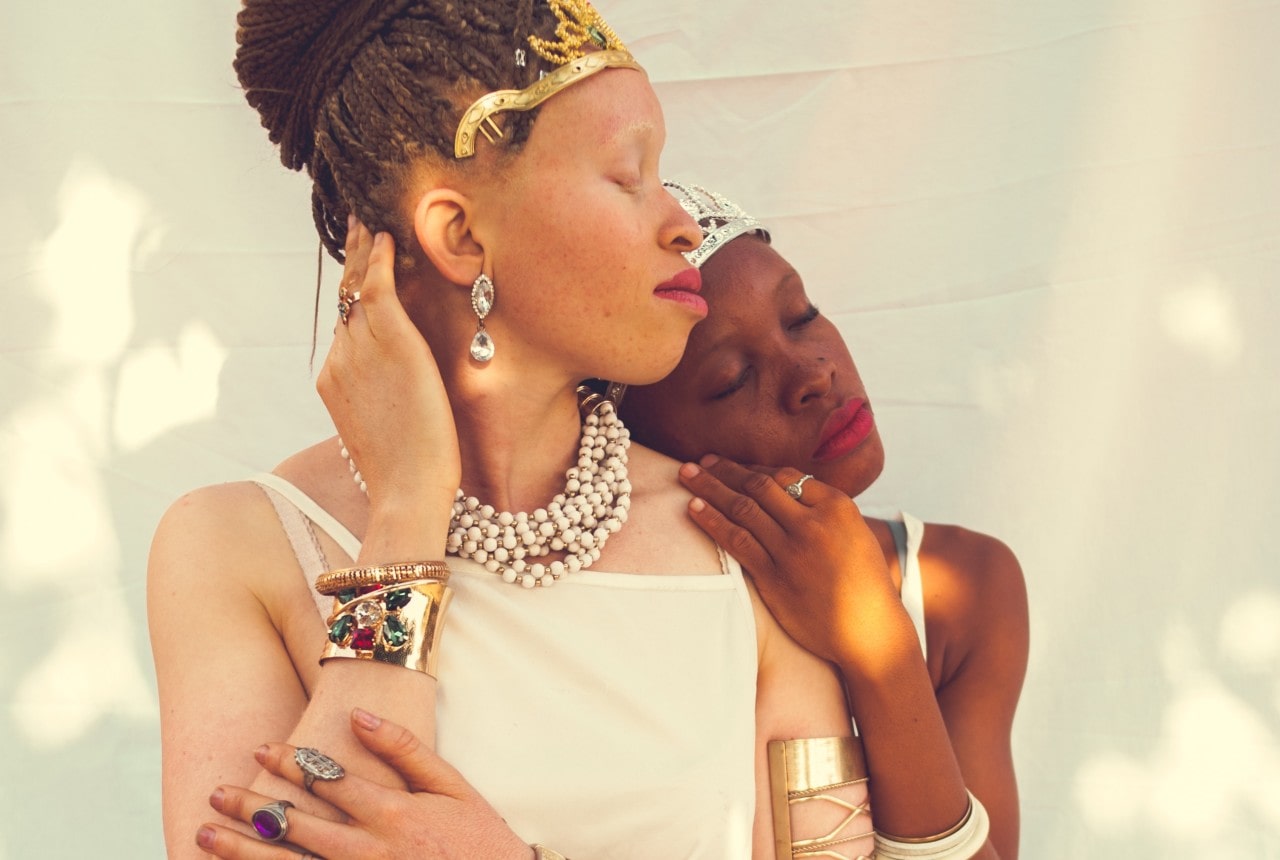 Two women wearing crowns, bracelets, rings, earrings, and necklaces