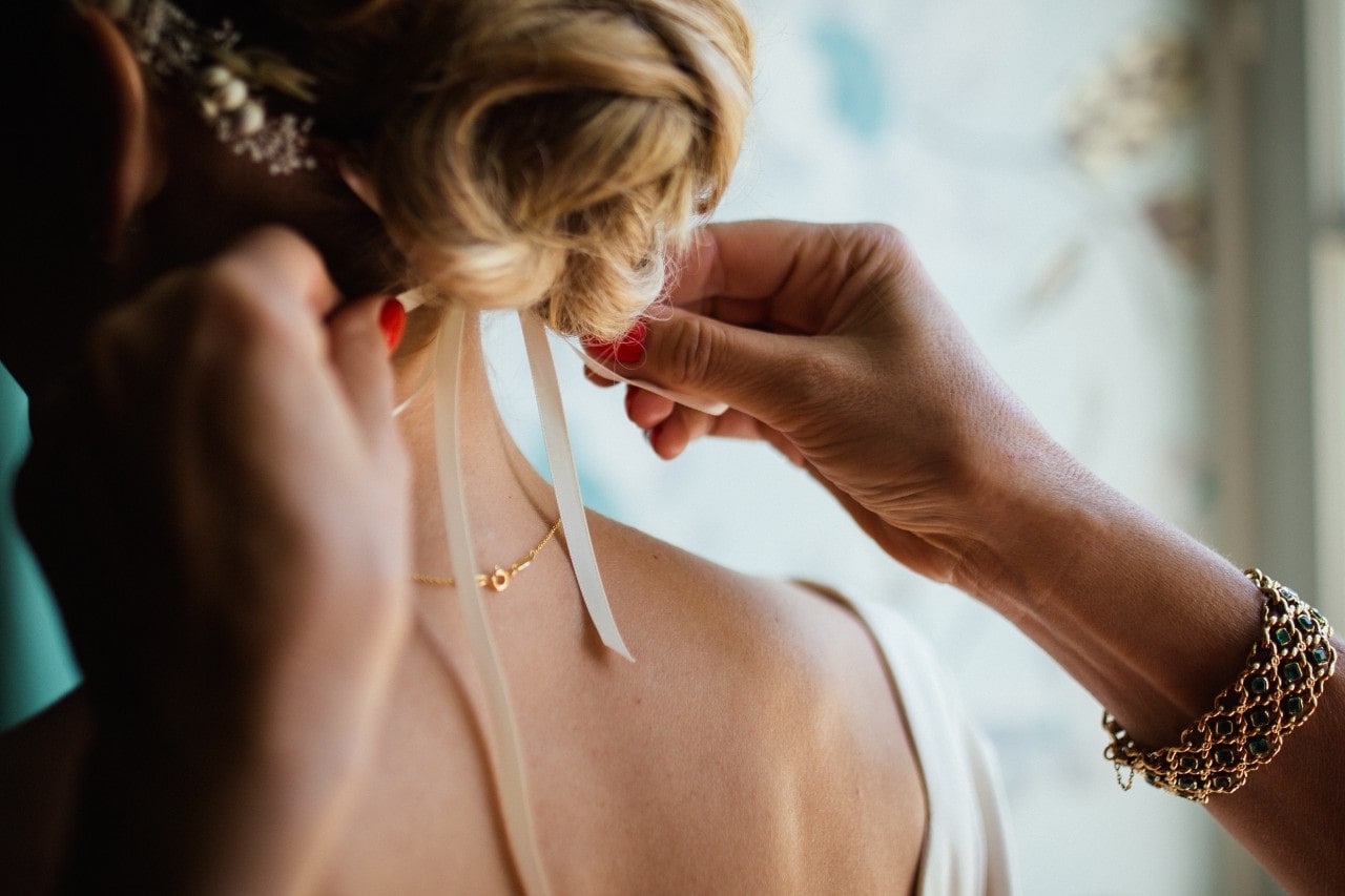 Bridesmaid helping the bride put on her jewelry