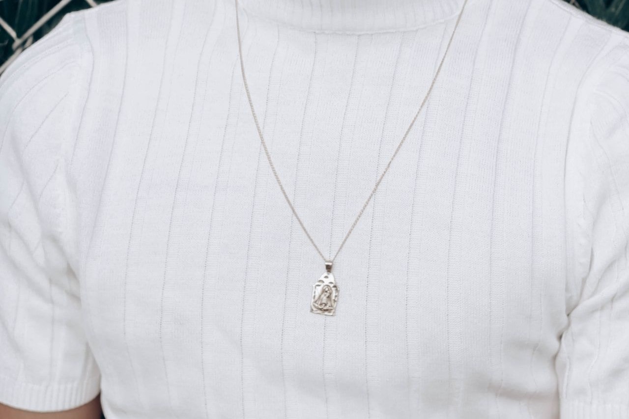 A woman wearing a white turtleneck sports a white gold chain necklace with a pendant