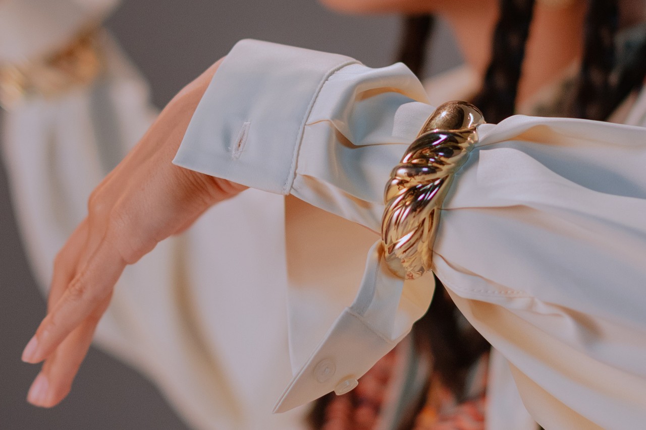 A woman slides a gold bangle over her white dress shirt’s sleeve