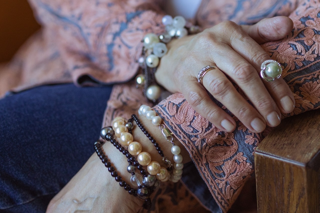 A woman wearing a cardigan with multiple bracelets sits in a chair