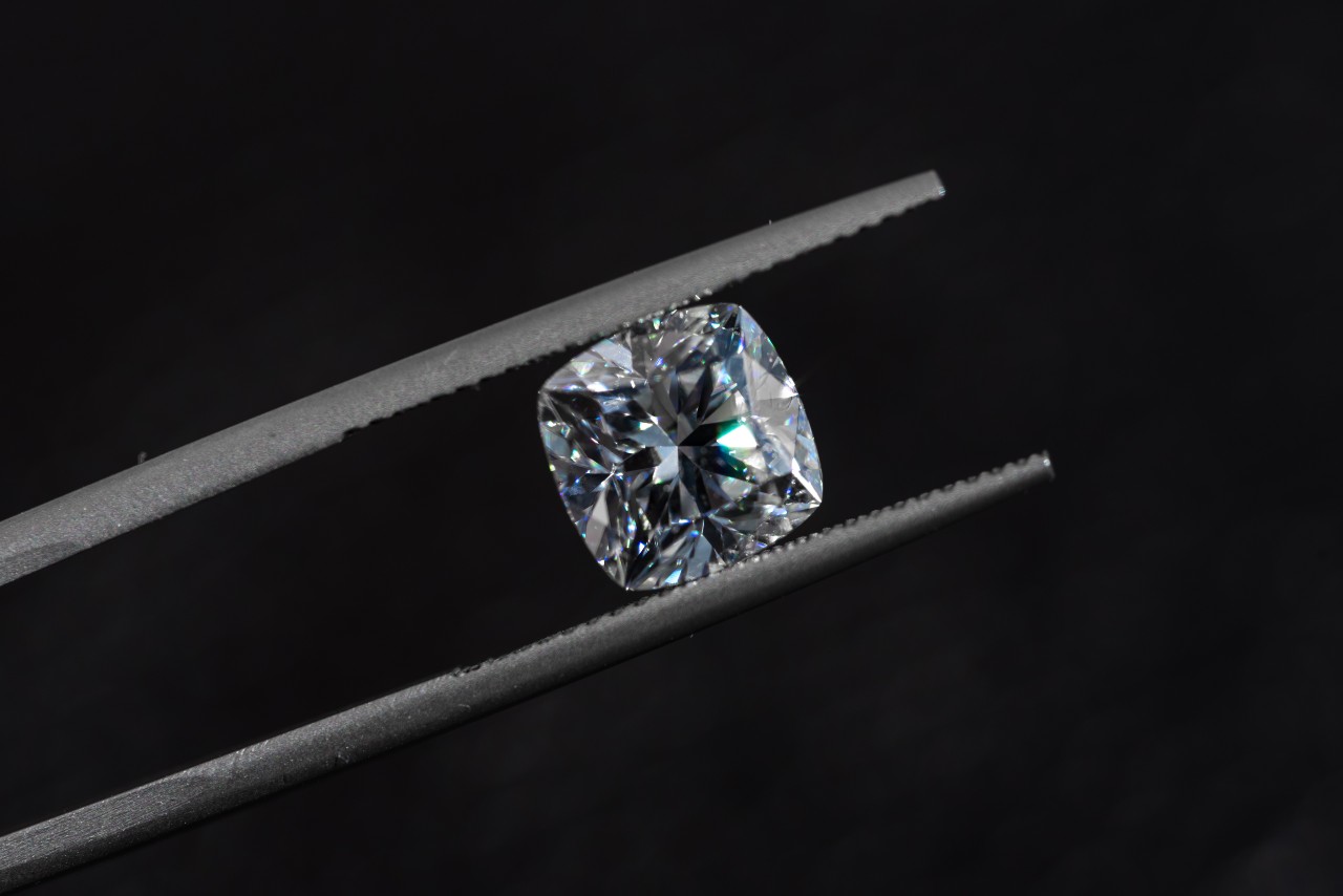 A cushion-cut diamond sits in a pair of jeweler tweezers