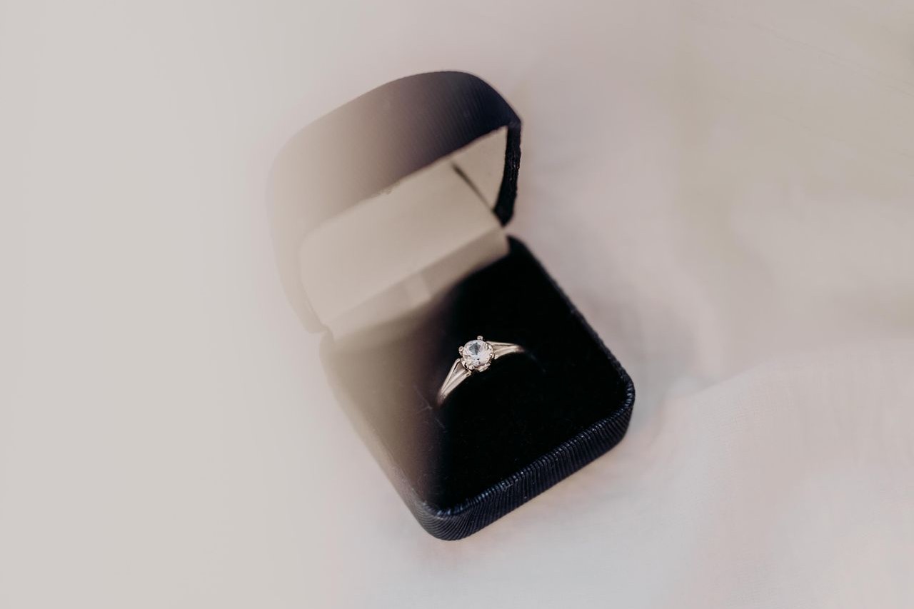 A solitaire engagement ring sits in a black box on a linen surface