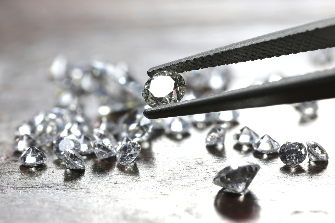 A jeweler inspects various diamonds on a gray wooden table