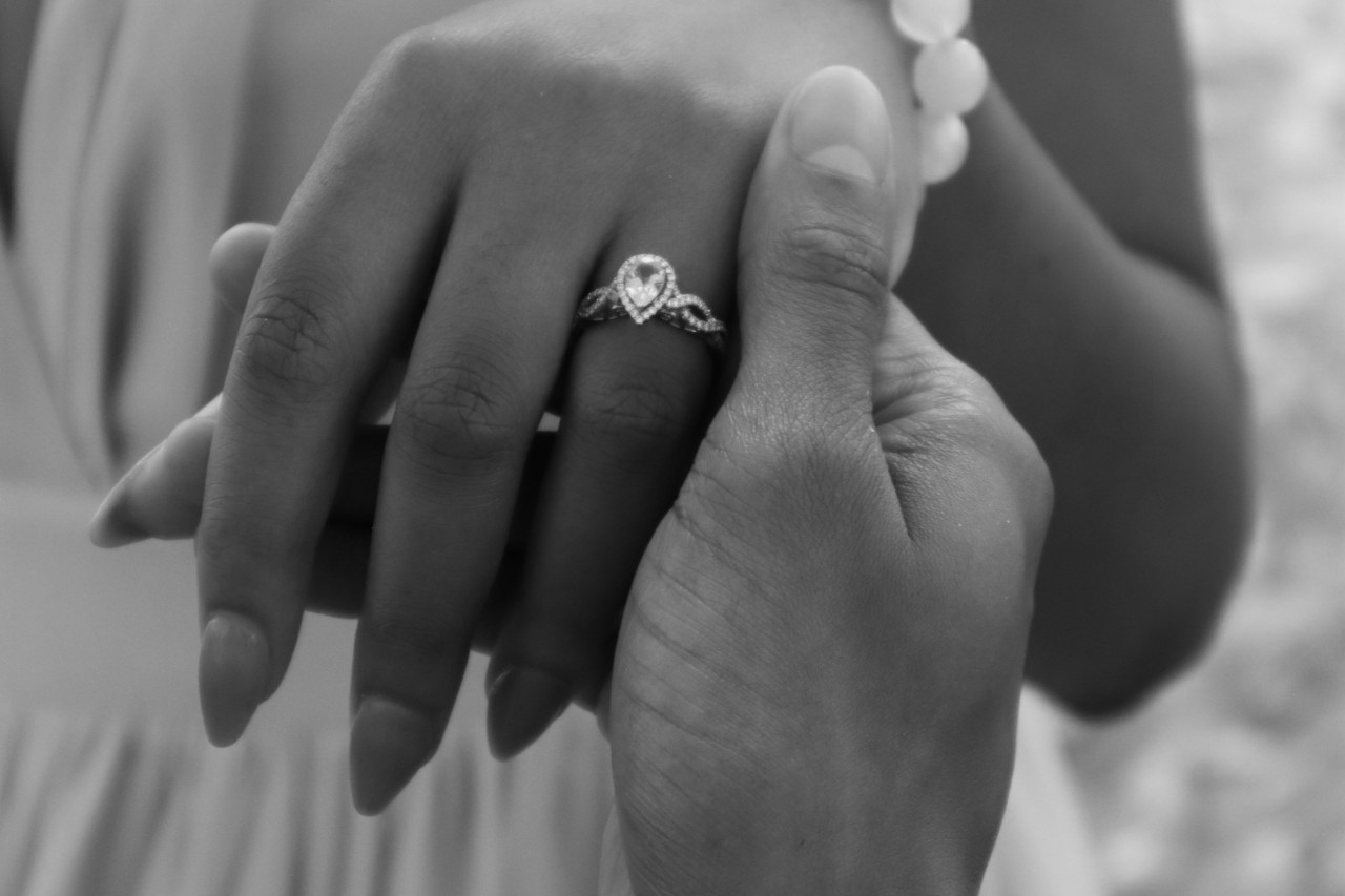 A man’s hand holding his bride-to-be’s, adorned in a pear shape engagement ring.