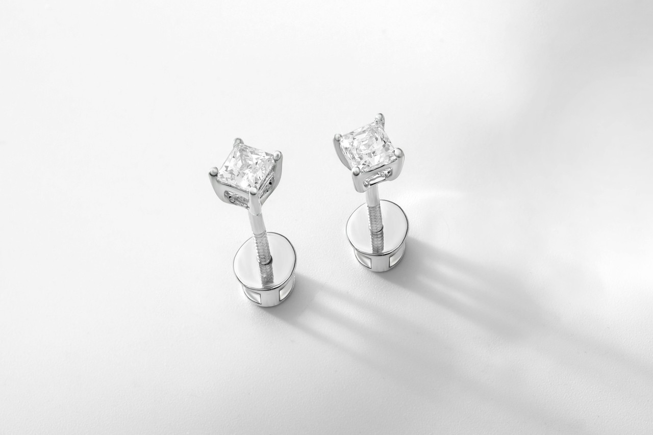 An elegant pair of diamond stud earrings on a white background.