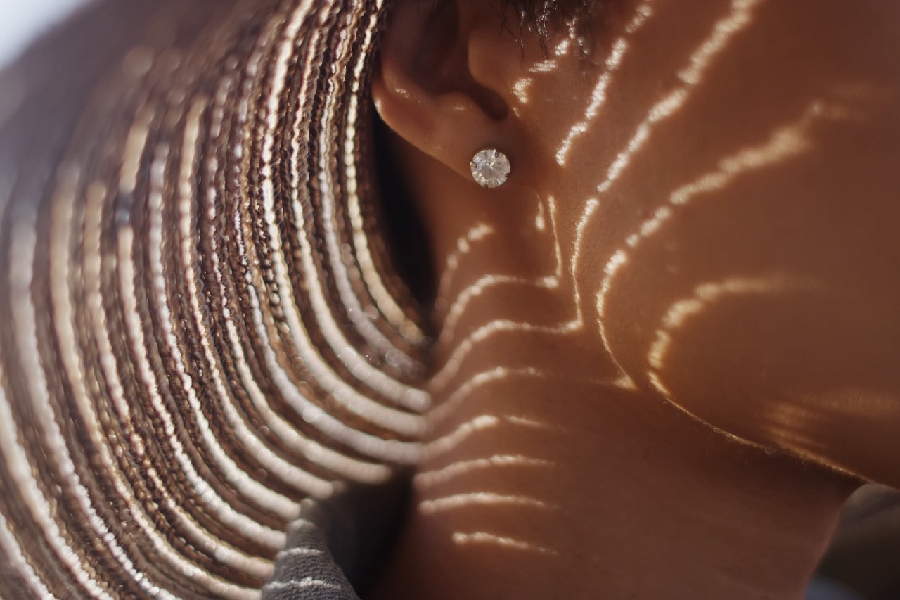 a close up of a woman’s ear sporting a diamond stud earring with a giant sun hat.