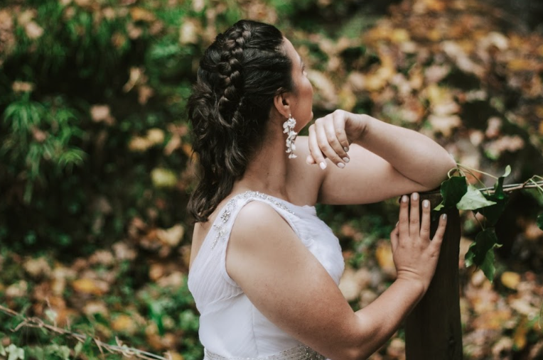 A bride with ornate drop earrings and braided hair looks back at autumn scenery.