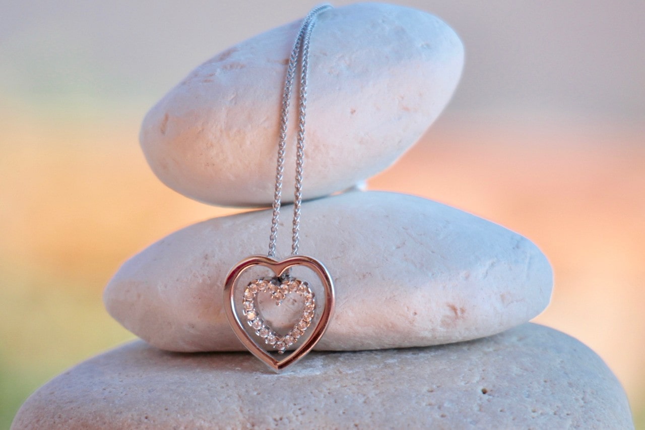 An elegant heart necklace displayed on three smooth, stacked stones.