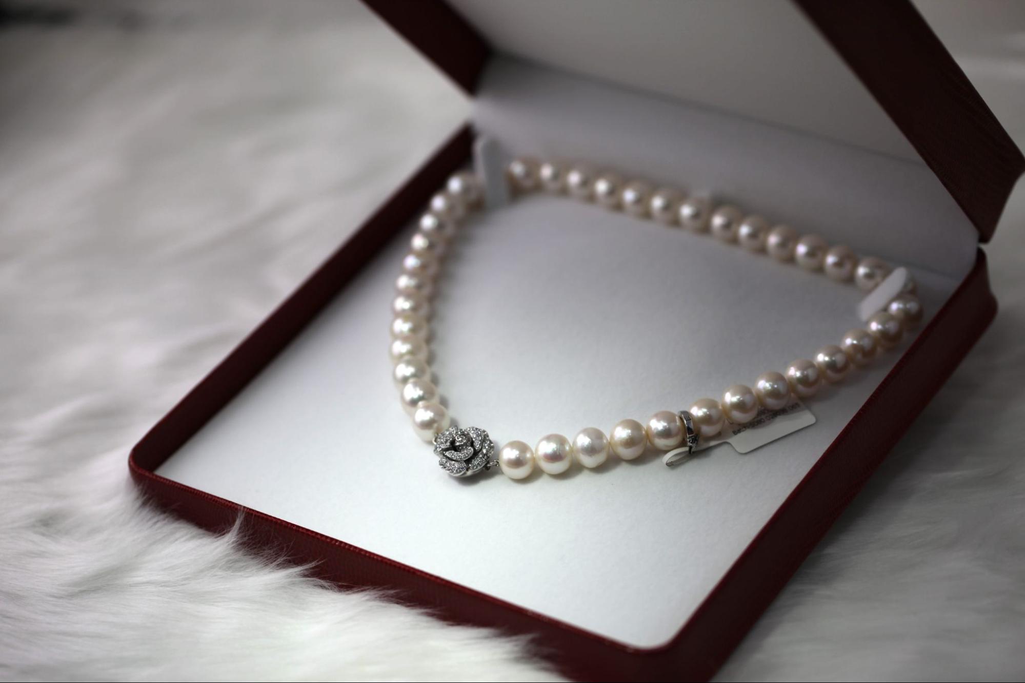 A close-up of an exquisite pearl necklace with a rose charm, displayed in-box on white fur.