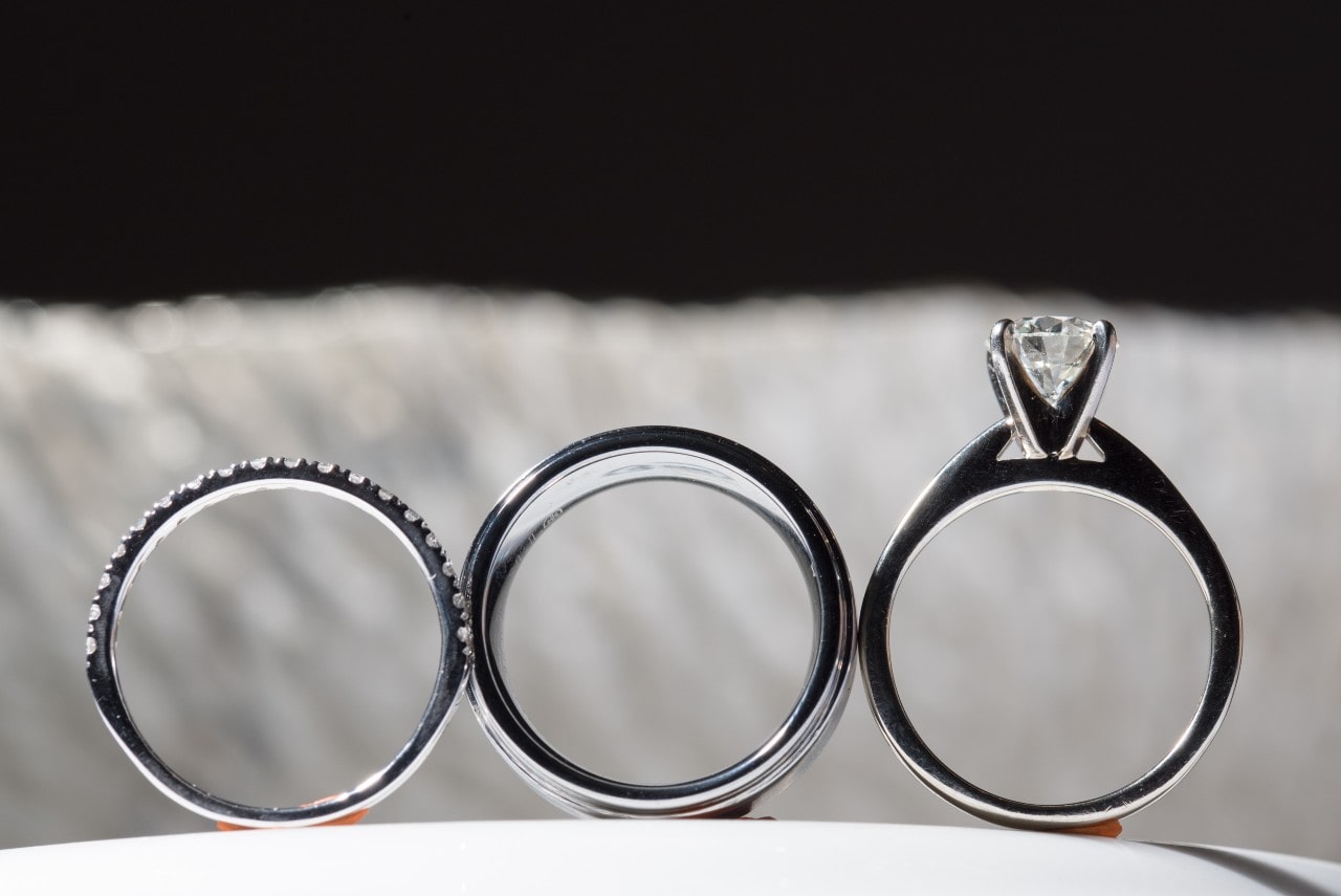 Three engagement rings, one diamond band, one band without precious stones, and one with a large center stone, displayed side-by-side