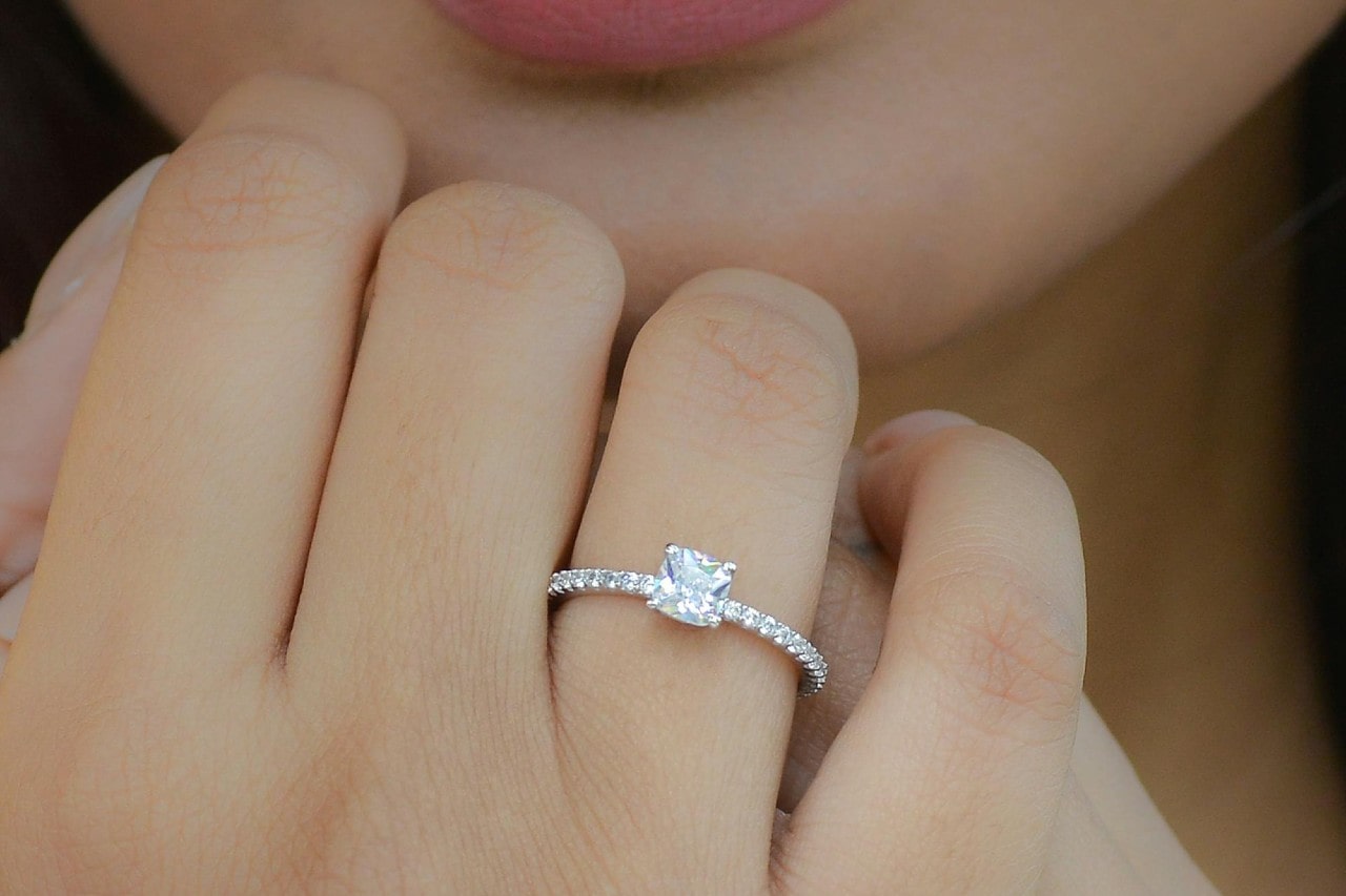 A close-up of a brilliant diamond engagement ring on a woman’s finger, her hands gently clasped in front of her chin.