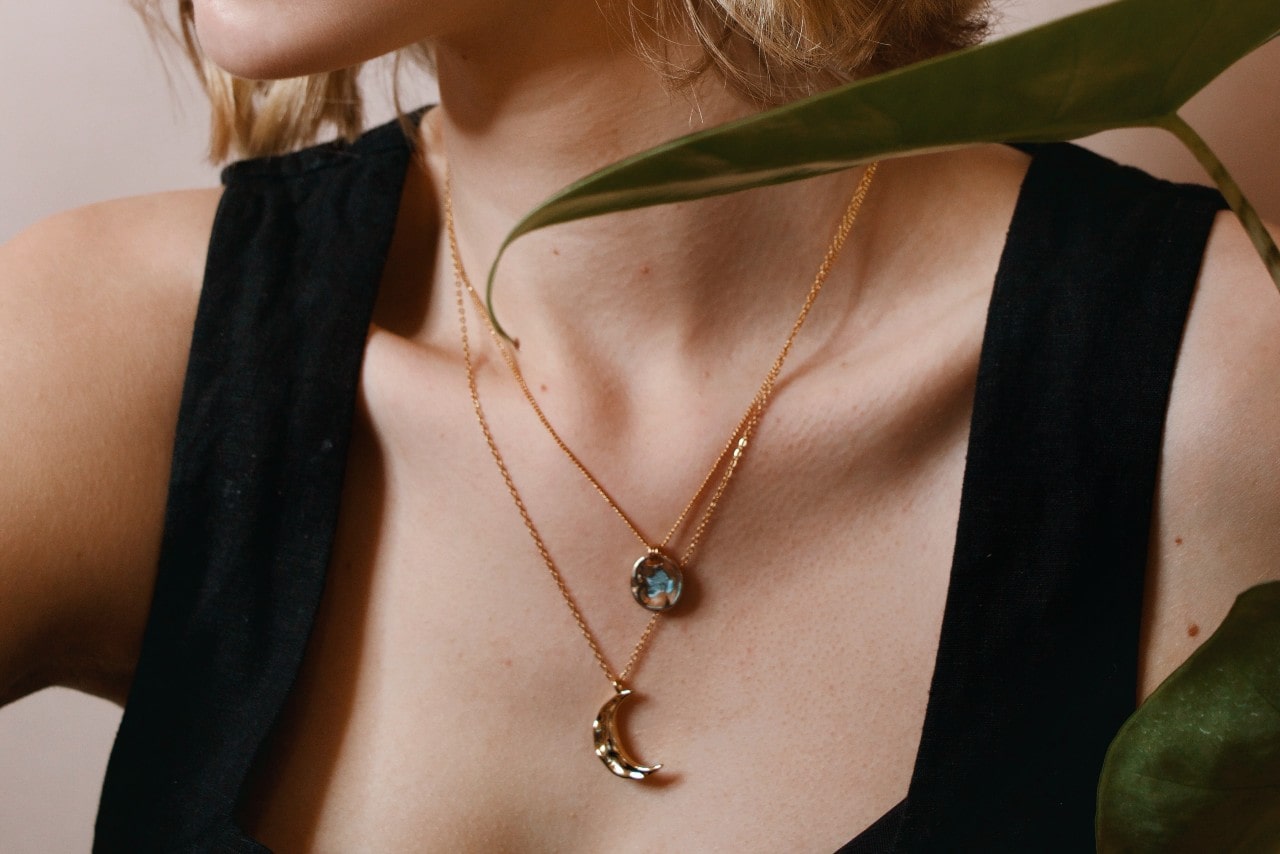 a woman wearing a black top and two rose gold pendant necklaces