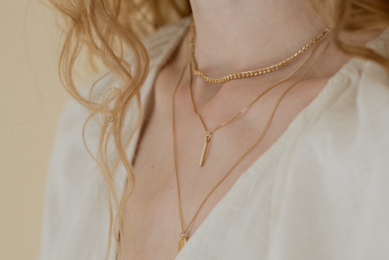 close up image of a woman’s neckline adorned with three gold necklaces of varying lengths