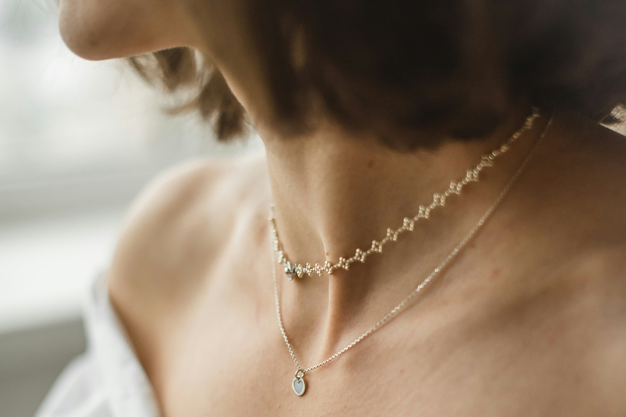 close up image of a woman looking away from the camera and wearing two fine chain necklaces