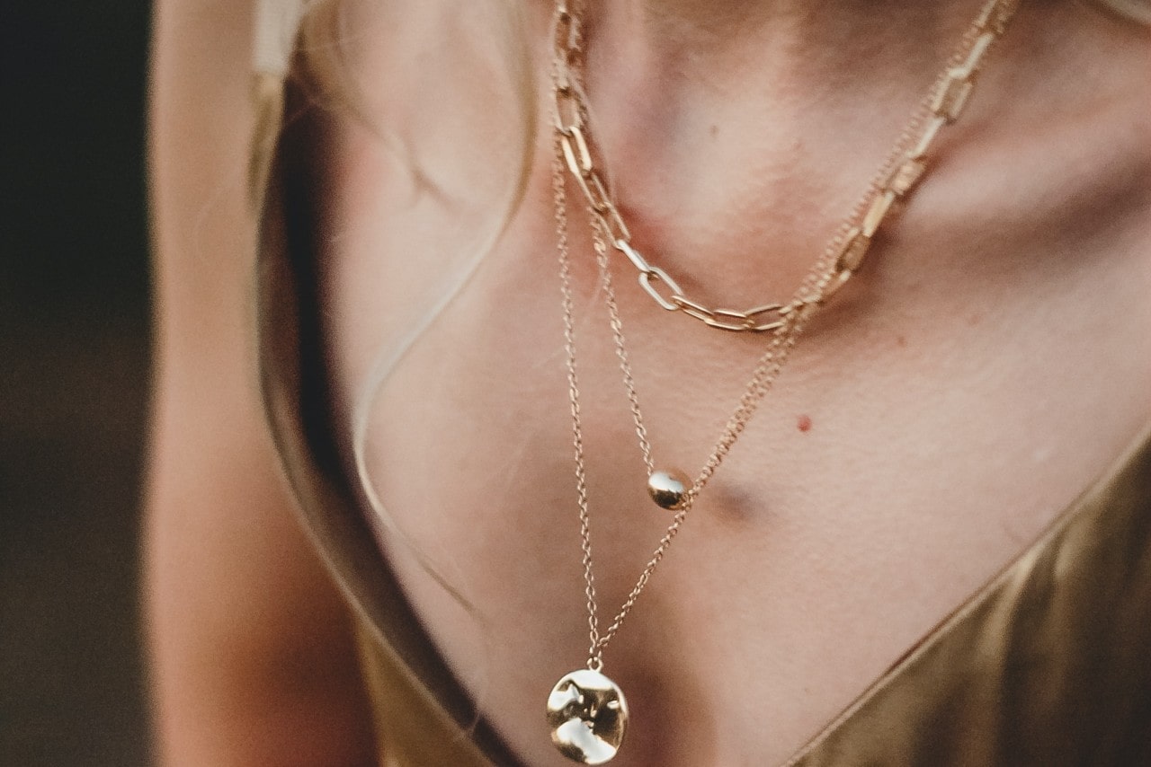 close up image of a woman’s neckline adorned with three gold necklaces layered