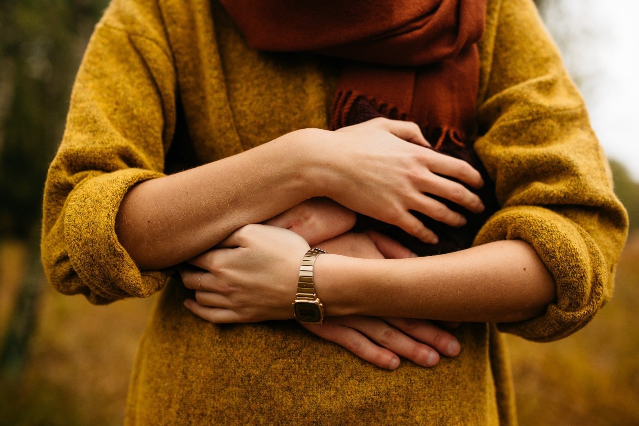 A close-up of a man wearing a gold watch hugging his partner from behind on a lovely fall day.