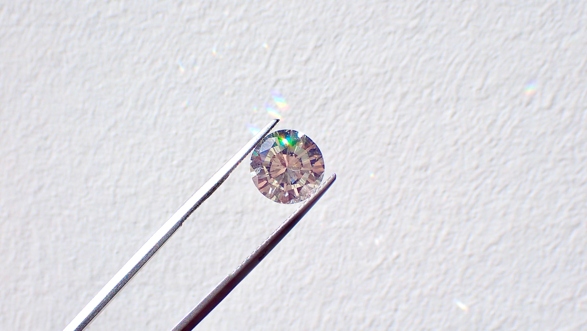 a round cut diamond held between tweezers against a white surface