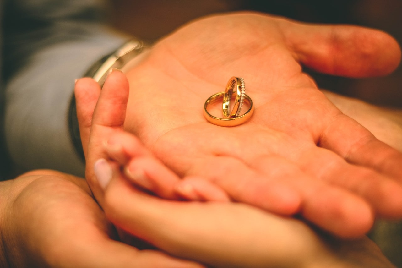 a man’s hand holding two wedding bands