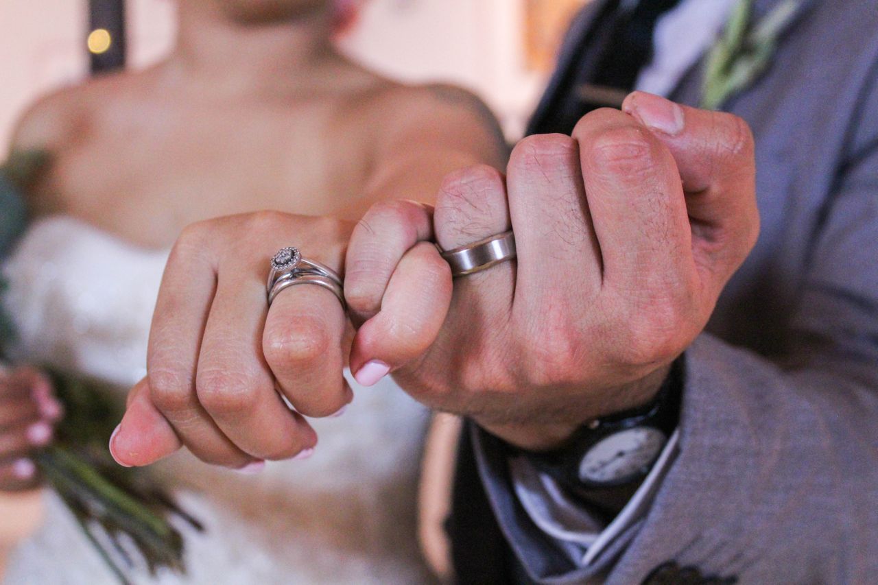 a bride and groom holding hands with pinkies interlocked and wearing bridal rings