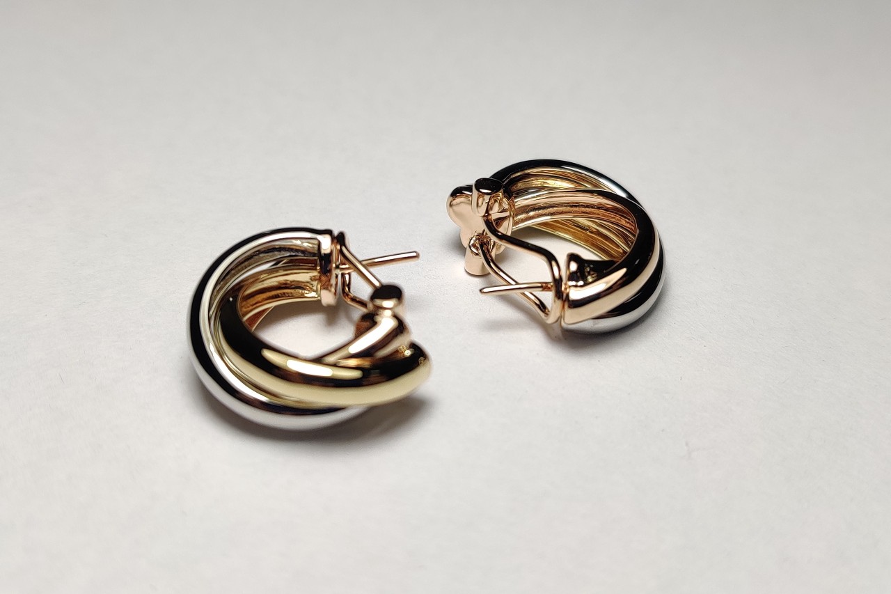 A pair of two-toned gold huggie earrings displayed on their sides on a pale backdrop. A pair of two-toned gold huggie earrings displayed on their sides on a pale backdrop.