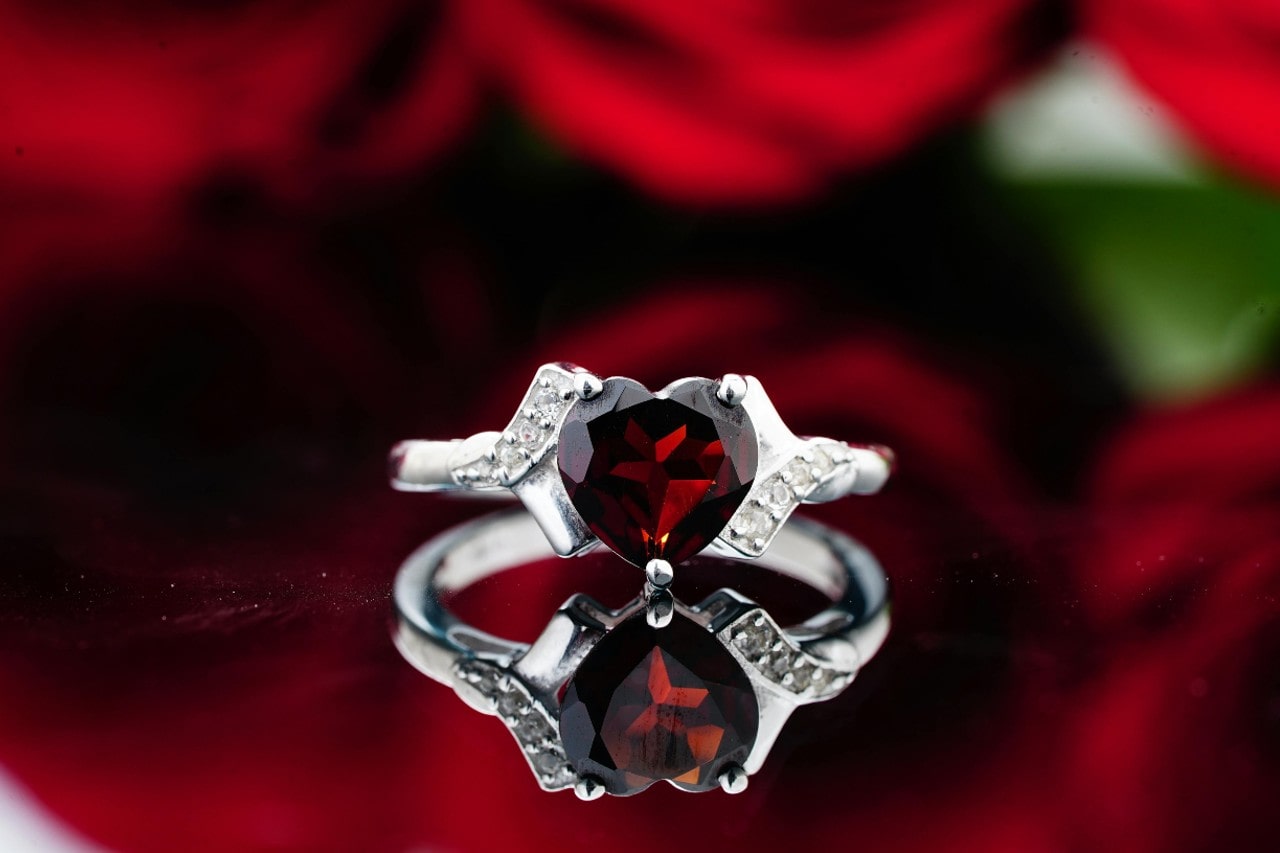 A close-up of an elegant ruby engagement ring displayed before a bouquet of roses.