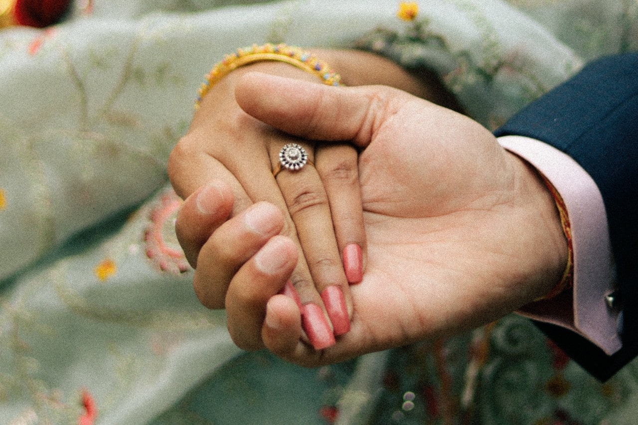 A close-up of a couple holding rings, with emphasis on the bride-to-be’s engagement ring.