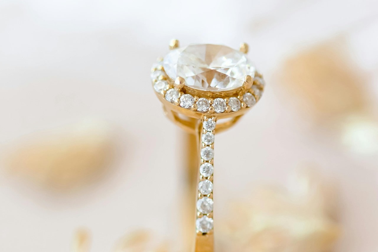 A close-up of a stunning yellow gold halo-set engagement ring with a side stone band.