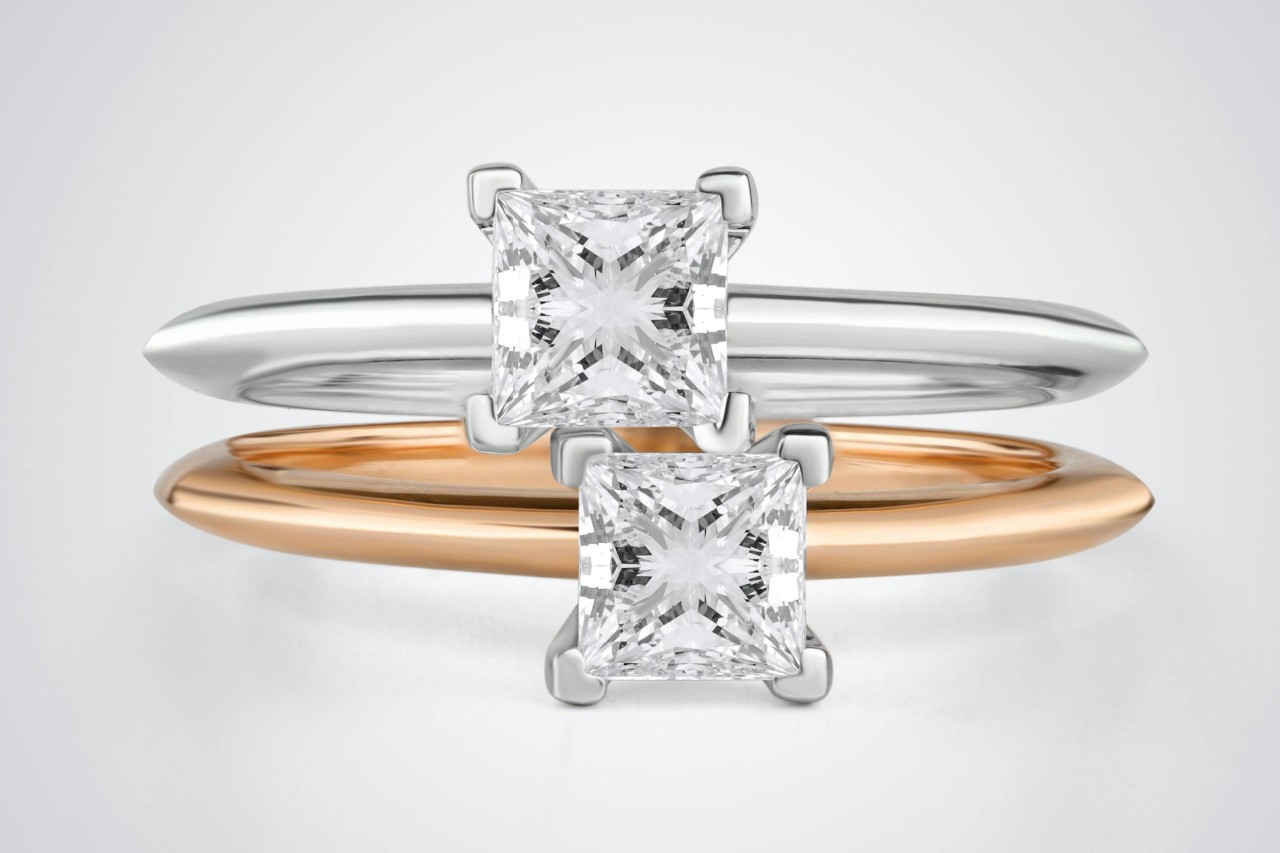 Two princess cut solitaire rings, one white gold and the other rose gold, stacked one on top of the other.