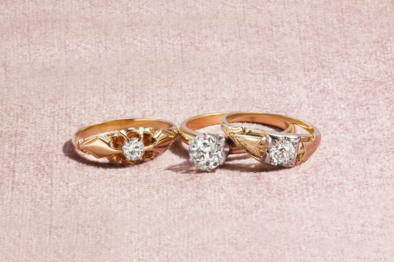 Three yellow gold diamond rings on a textured pink surface.