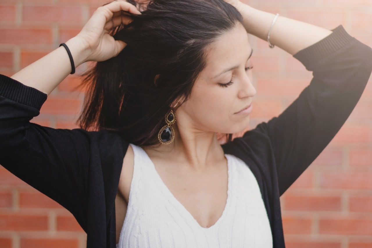 a lady brushing her hair back with her hands, wearing gemstone earrings