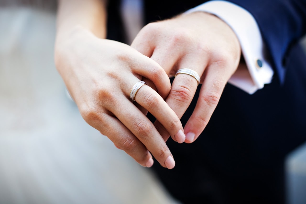 A bride and groom’s hands, wearing matching matte wedding bands.