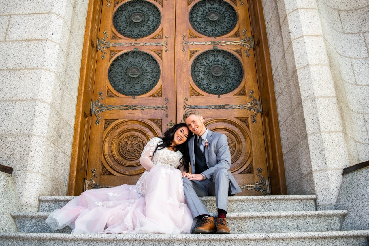 A bride and groom sitting together on the steps outside a church.