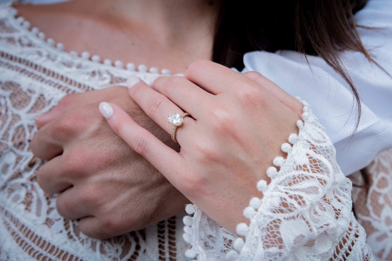 A bride holds her groom’s hand.