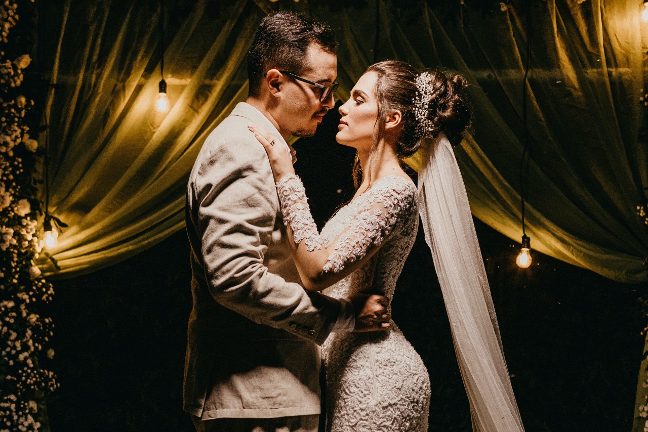 a bride and groom embracing in front of a dimly lit curtain