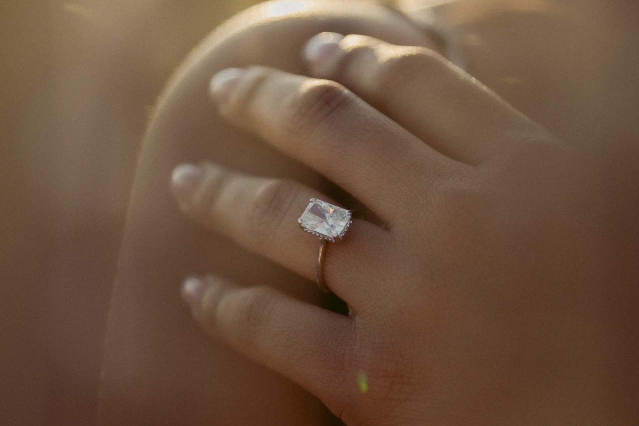 a lady’s hand wearing an emerald-cut simple engagement ring